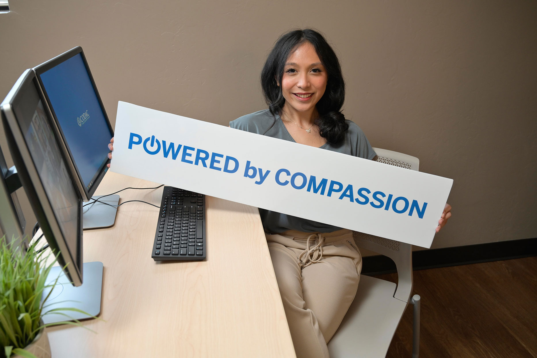 A Team Member Sitting at a Desk With a Powered by Compassion Sign at CODAC.