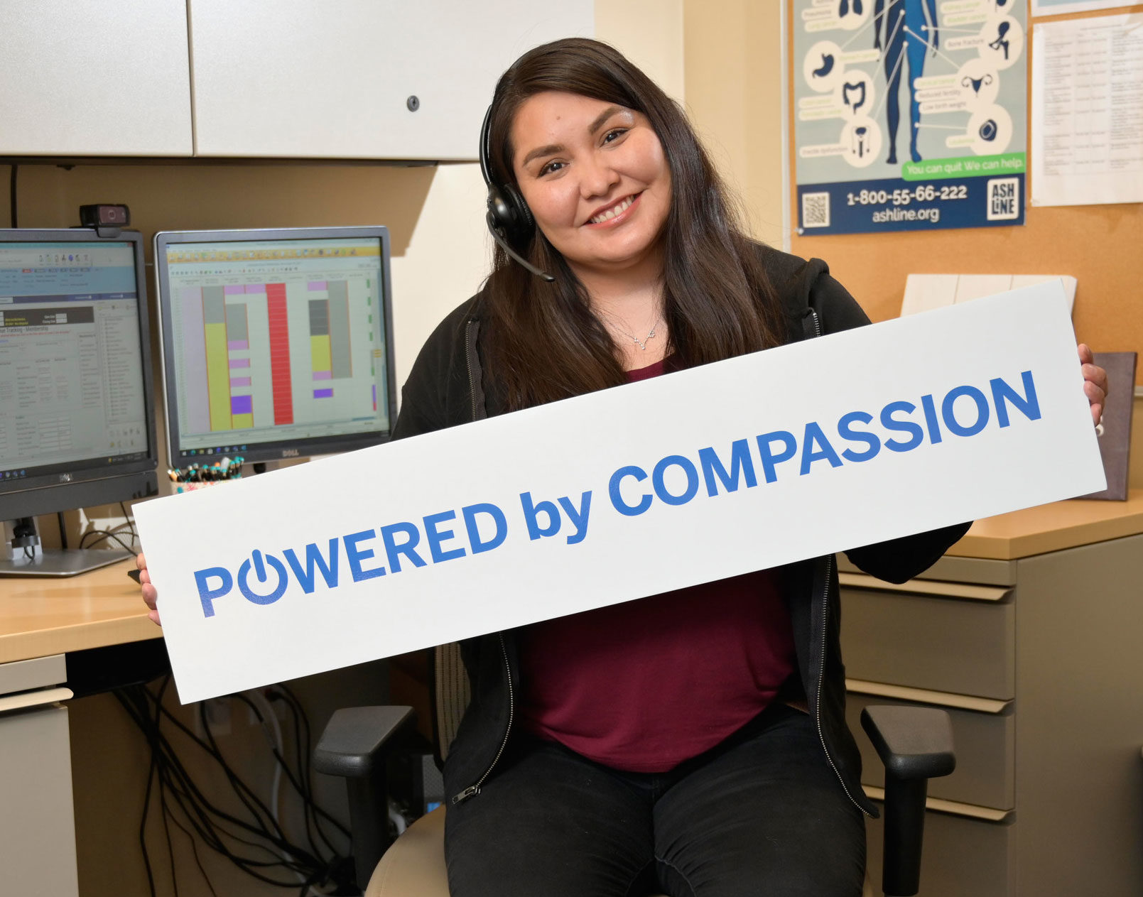 A CODAC staff member that reviews AHCCCS eligibility holding Powered by Compassion sign.
