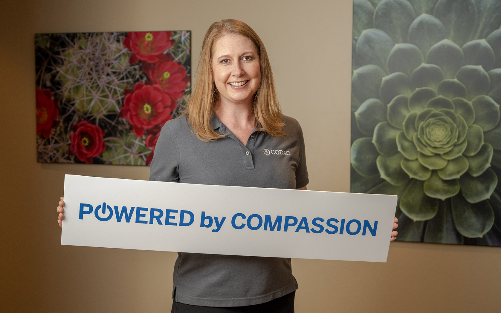 A Woman Holding a Powered by Compassion Sign at CODAC Office.