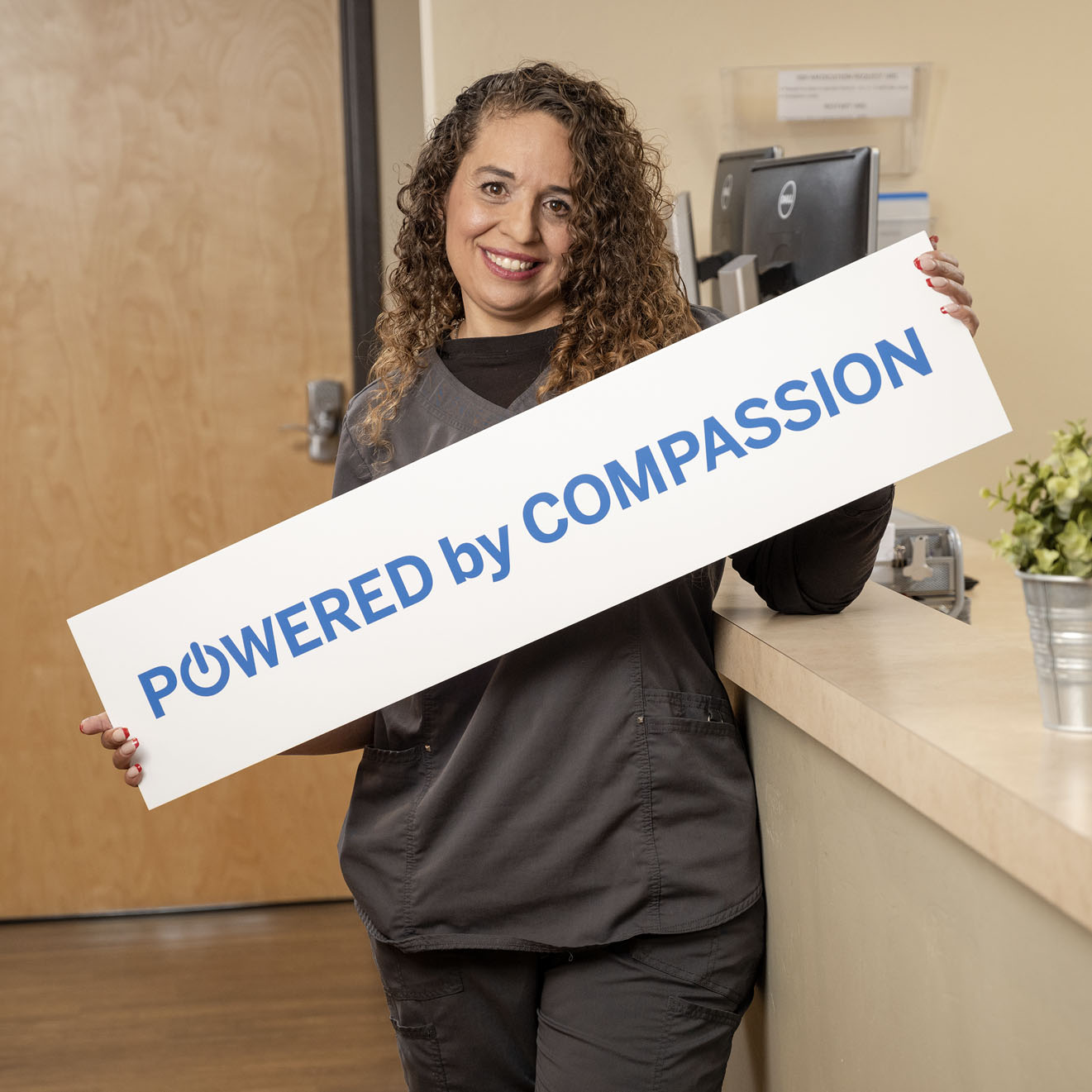 Team Member Holding a Powered By Compassion Sign at CODAC Office.