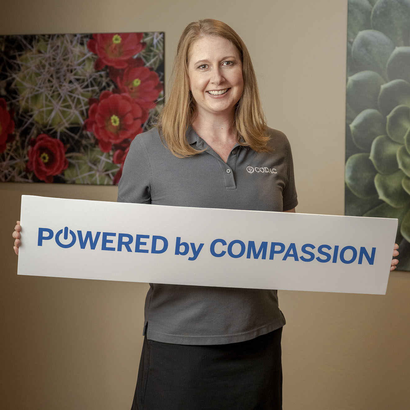 A Woman Holding a Powered by Compassion Sign at CODAC Office.