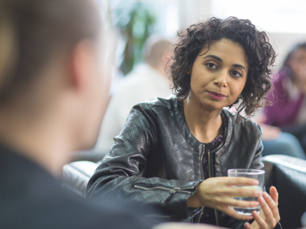 Female in conversation with another person, holding an alcoholic beverage.